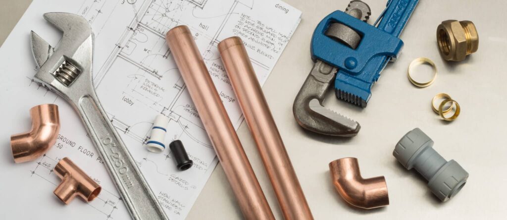 Showcase your plumbing expertise with a compelling display featuring copper pipes, an adjustable wrench, a blue pipe wrench, fittings, and detailed plumbing diagrams. Perfect for plumbing marketing agencies looking to highlight their skills and professionalism.