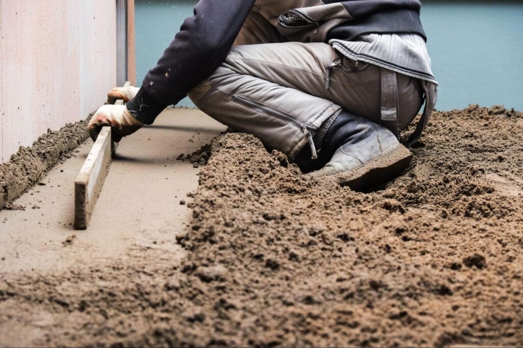 A worker kneels, leveling fresh concrete with a screed tool, demonstrating precise technique essential for foundation repair.
