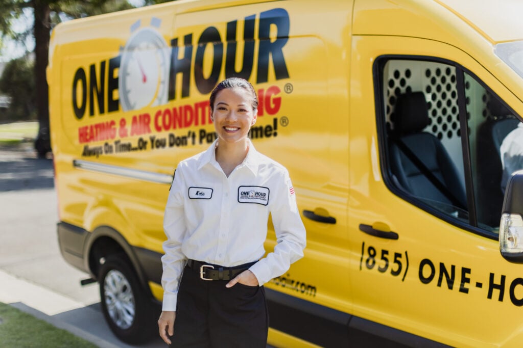 A One Hour Heating & Air Conditioning technician stands in front of a bright yellow van, proudly representing one of the Top 10 HVAC companies in the U.S.