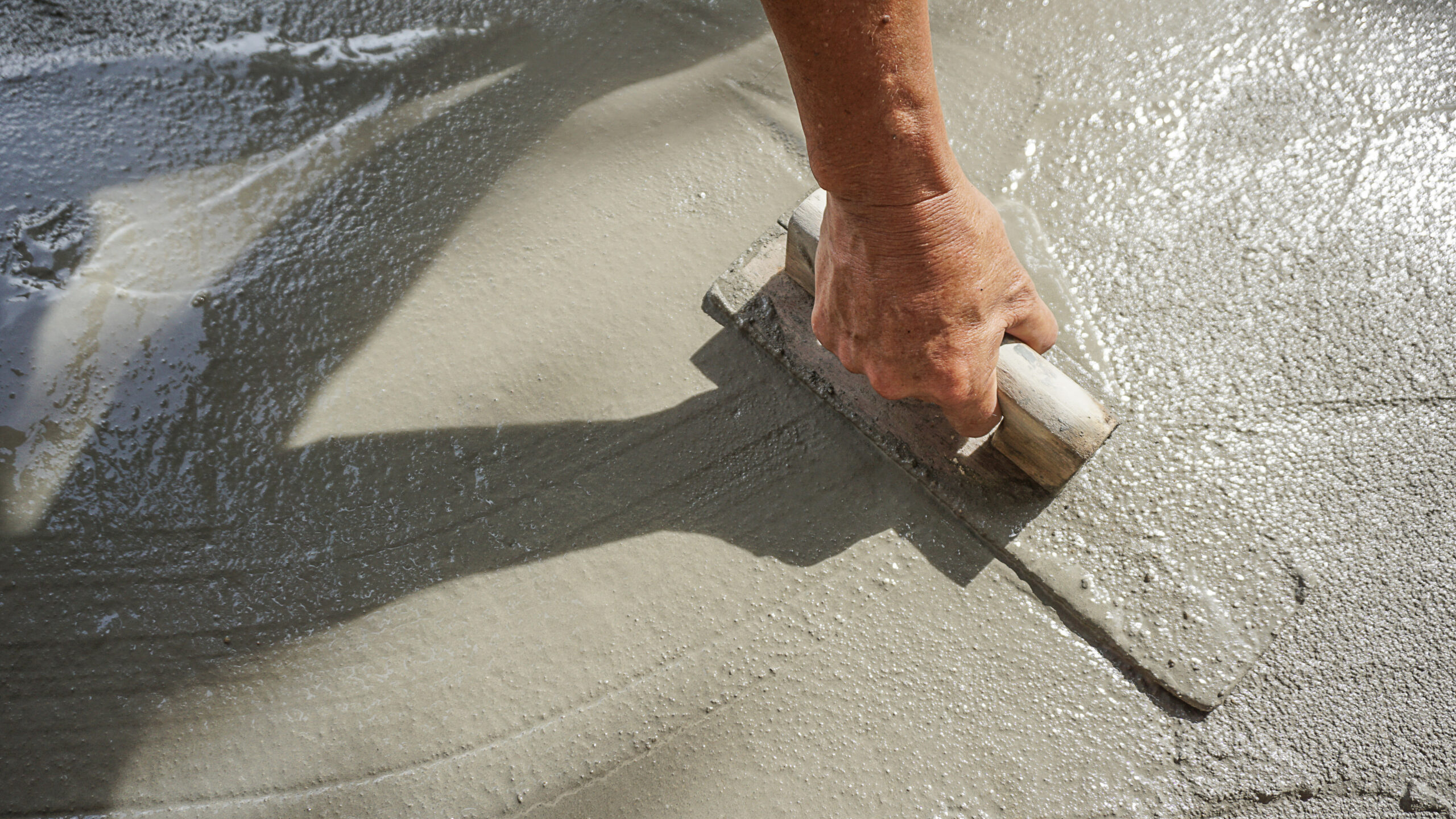 A skilled worker expertly smooths wet cement with a trowel, showcasing professional hardscaping techniques. The close-up highlights the precision and finesse required to achieve a flawless concrete finish.