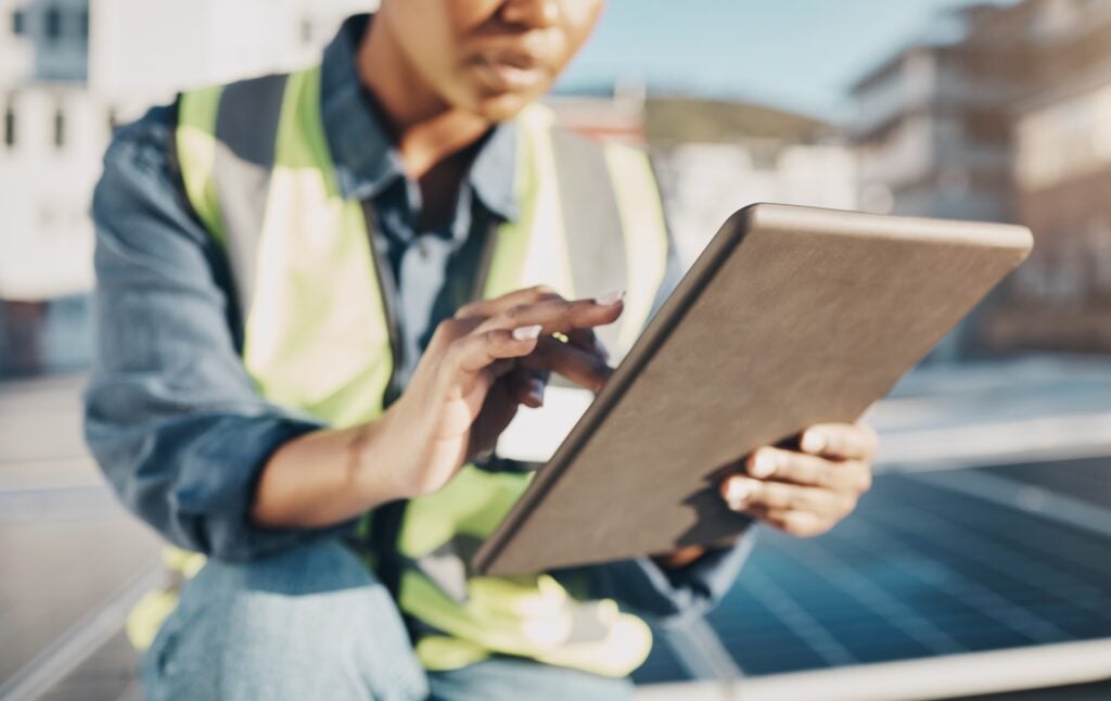 A professional in a safety vest conducts a digital roof inspection with a tablet at a solar panel installation site, demonstrating modern, tech-driven alternatives to traditional inspections.