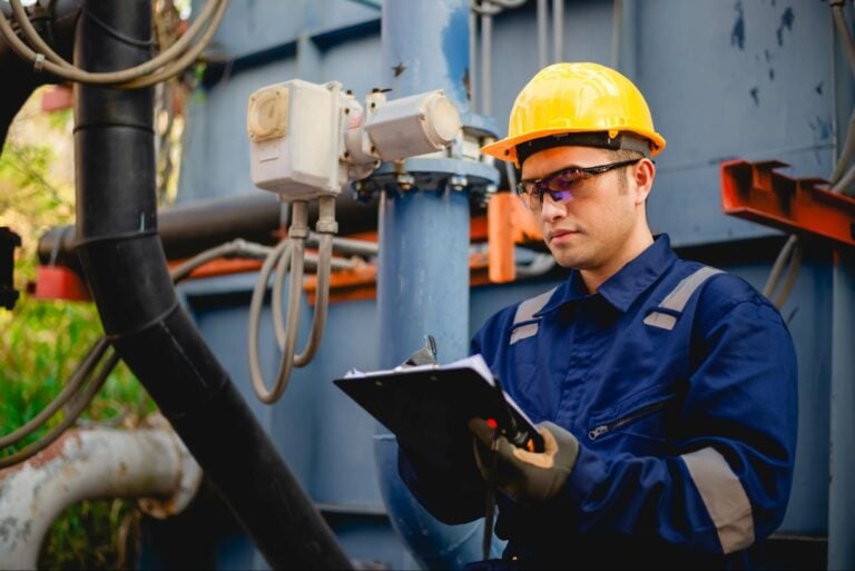Industrial worker in PPE inspects equipment and records data at an outdoor facility serving homeowners—Hook Agency project in action.