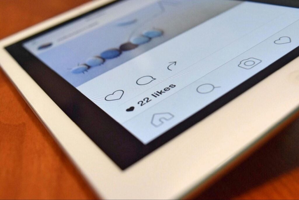 Tablet displaying an Instagram post with 22 likes; like, comment, and share icons visible. Device sits on a wooden surface.