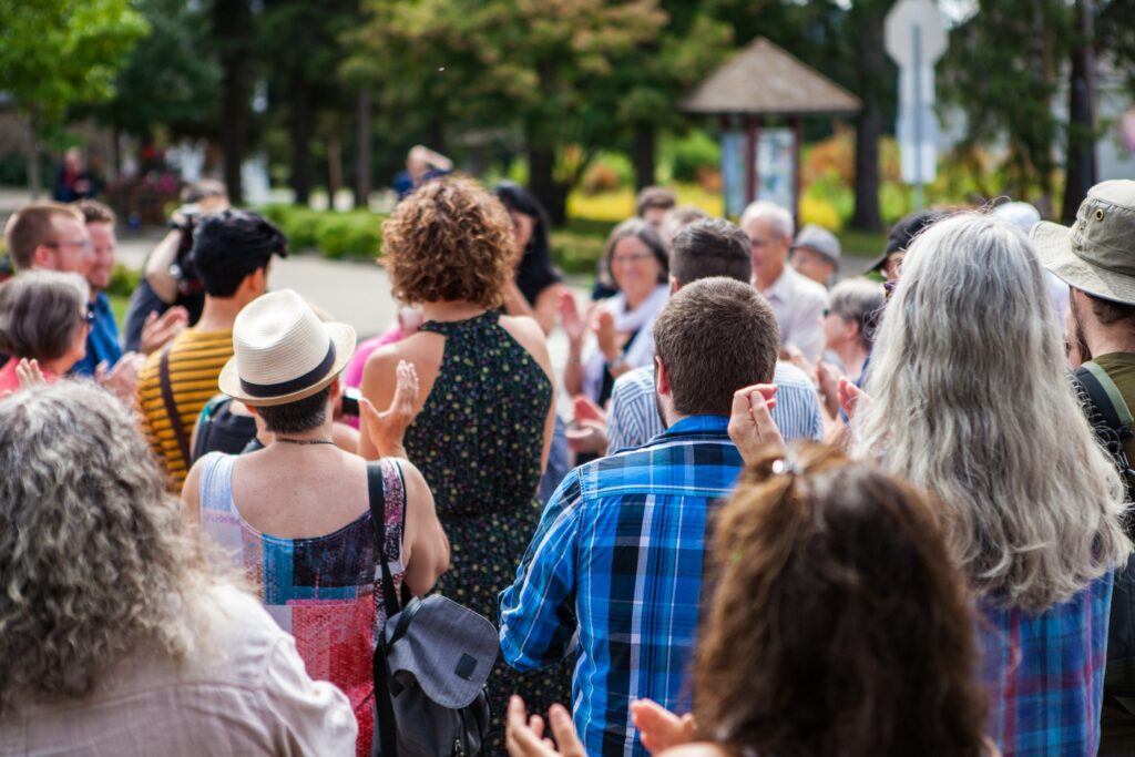 A diverse group of homeowners stands together outdoors, applauding amid vibrant greenery. This lively, welcoming scene is ideal for promoting 2025 community events or enhancing your next Facebook targeting campaign.