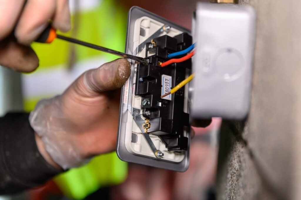 Male hands wiring a uk socket plug on garage wall with screw driver with rubber gloves