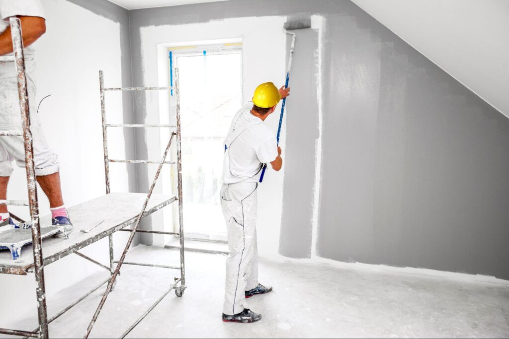 Professional contractors in safety gear efficiently paint a protected room, demonstrating thorough preparation and expertise.