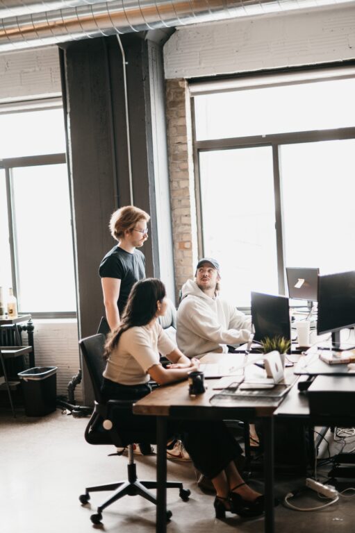 Team strategizing HVAC LSA management in a bright, modern office at Hook Agency; two at computers, one leading discussion.