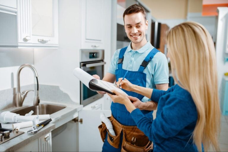 Plumber in blue overalls presents paperwork to a client signing in a modern kitchen, highlighting effective referral marketing.