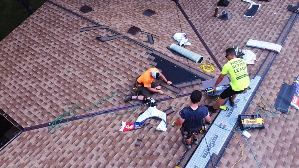 Aerial view of three roofers installing shingles, using proper tools and safety gear on a residential project for a roofing business.