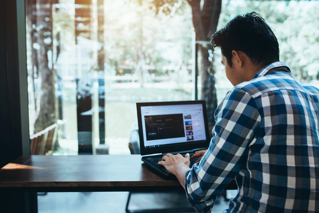 On Hook Agency's website, an individual in a checkered shirt conducts user testing strategies on a laptop at a wooden table. The room is bright, with large windows showcasing trees and daylight outside.