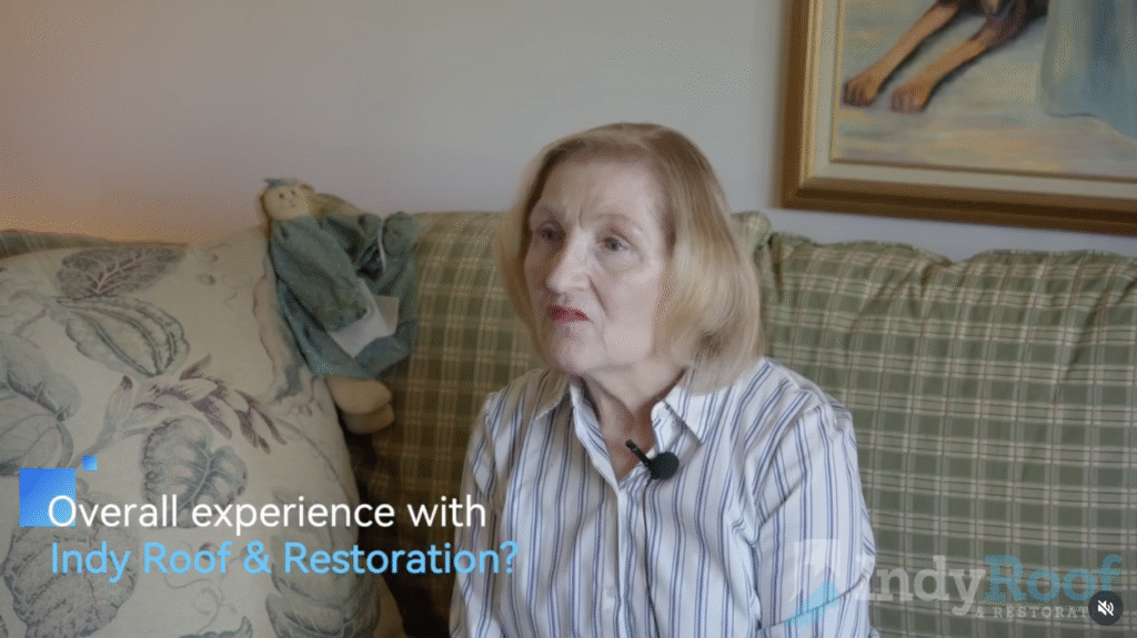 A testimonial video features an older woman with light hair, seated on a plaid couch and wearing a striped shirt with a lapel microphone. The on-screen text asks, "Overall experience with Indy Roof & Restoration?" This video exemplifies effective short-form video marketing by roofers. The background includes a doll and a painting, adding authenticity to the setting.