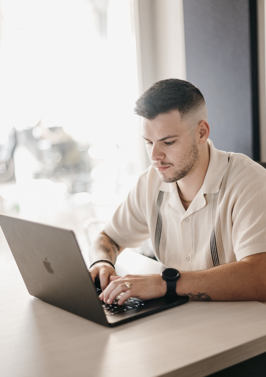 On-page SEO for HVAC Companies - A professionally groomed man studies patio contractor SEO strategies on his laptop. Dressed in a striped white shirt and a smartwatch, he is focused and situated in a brightly lit indoor setting.