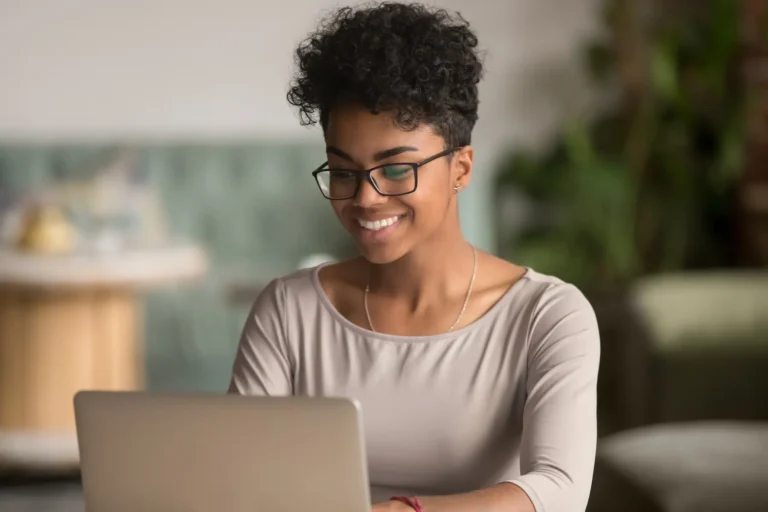 A person with short curly hair and glasses smiles while reviewing a contractor's website design on a laptop